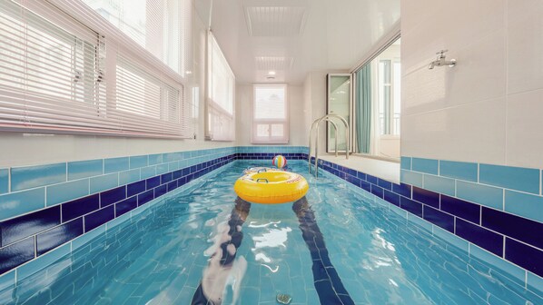 Une piscine aux carreaux bleus, un flotteur jaune et une porte en verre donnant sur un espace douche.