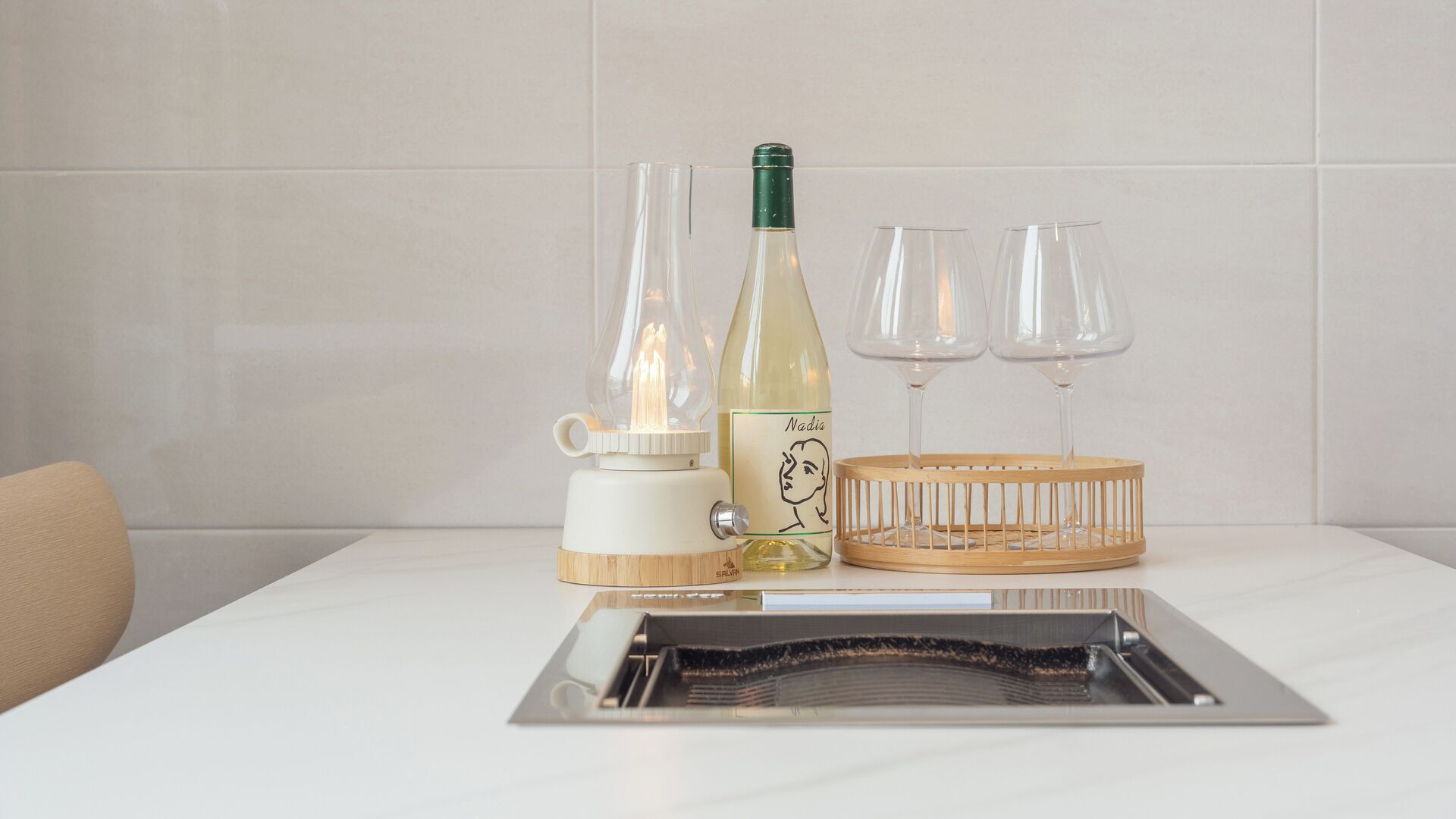 Una mesa blanca con una botella de vino, dos copas, un candelabro y una bandeja.