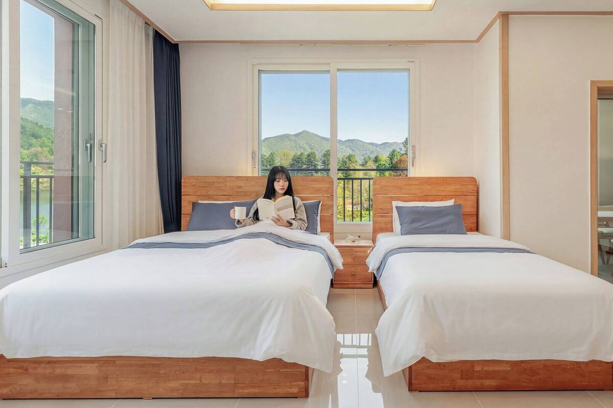 Habitación de hotel con dos camas, un balcón con vistas a las colinas y un comedor visible a través de un ventanal.