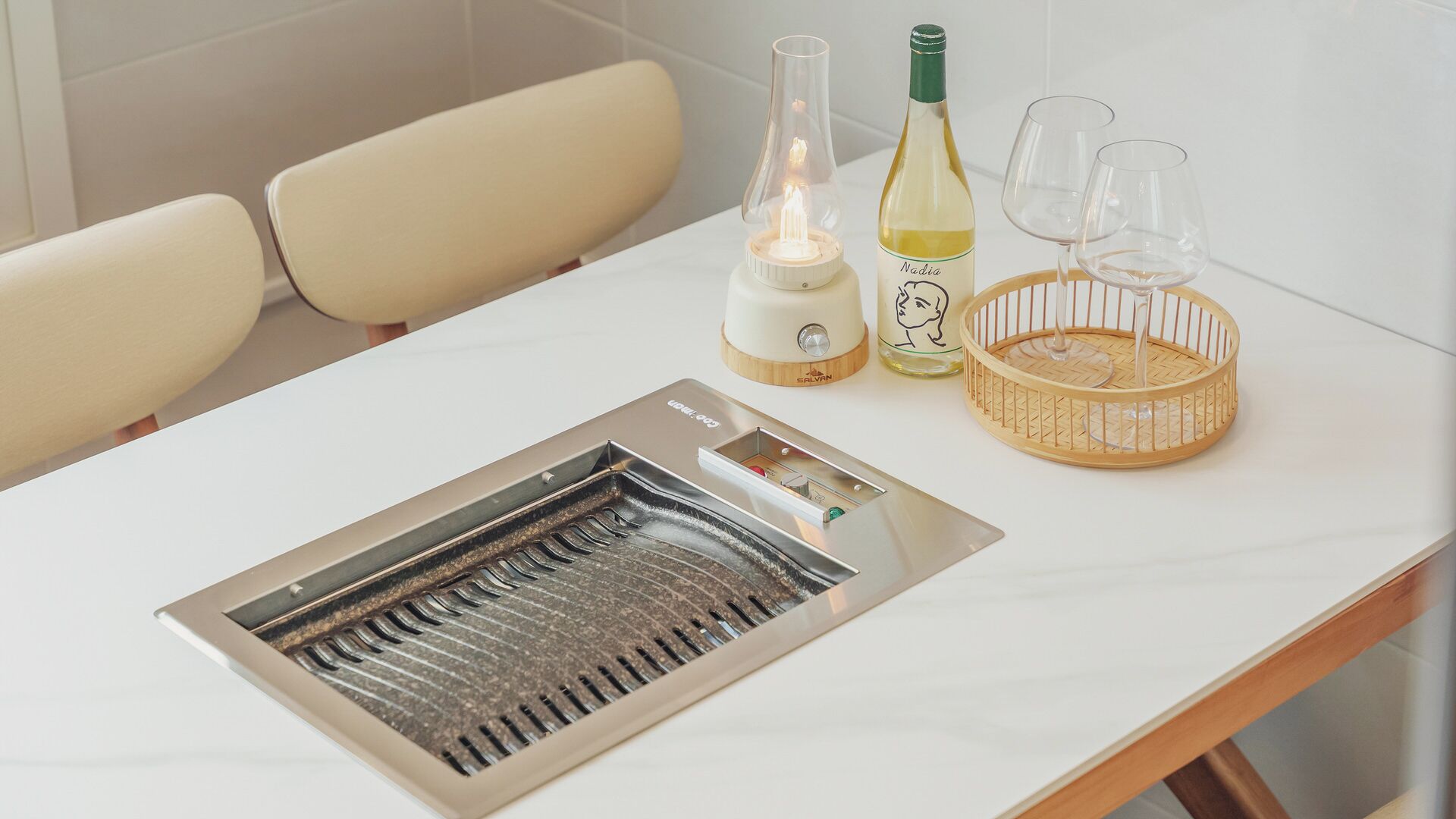 A table with a built-in grill, a bottle of wine, glasses, and a candle.