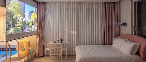 A hotel room with a bed, a small table with a drink, a chair, and a window with curtains.