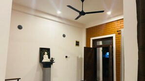 A room with a ceiling fan, a statue on a pedestal, a wooden bench, and a door leading to another room. - Eco Brick Transit villa  AC in Katunayake (Katunayake)