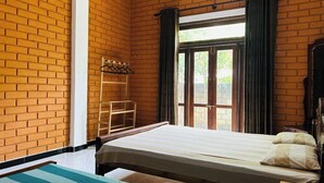 A room with a brick wall, a bed with a striped blanket, a wooden ladder, and a window with curtains. - Eco Brick Transit villa  AC in Katunayake (Katunayake)