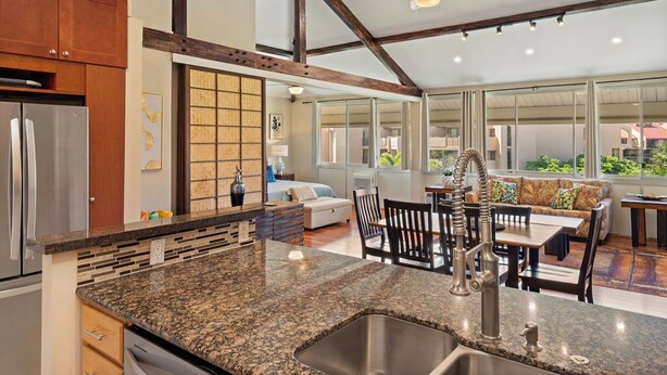 A modern kitchen with granite countertops, a stainless steel refrigerator, and a dining area with a table and chairs. - Haleakala Shores B512: Luxe top-floor with dual master suites. Steps to beach. (Kihei)