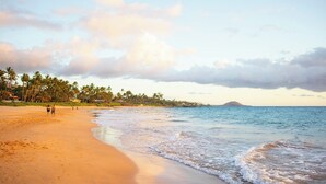 A beach with footprints, palm trees, and a distant island. - Haleakala Shores B512: Luxe top-floor with dual master suites. Steps to beach. (Kihei)