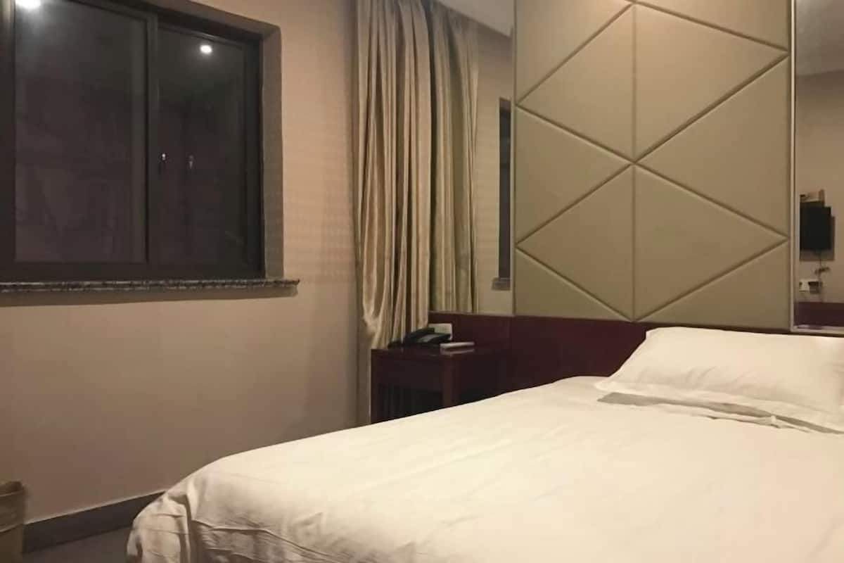 A hotel room with a bed, a nightstand, a mirror, and a window with curtains.