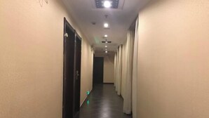 Un couloir d’hôtel avec un sol carrelé, une porte à gauche et des rideaux à droite.