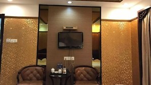 Une chambre d’hôtel avec un plafond en bois, un téléviseur à écran plat fixé au mur, deux fauteuils en cuir et une petite table sur laquelle se trouve un plateau avec divers objets.