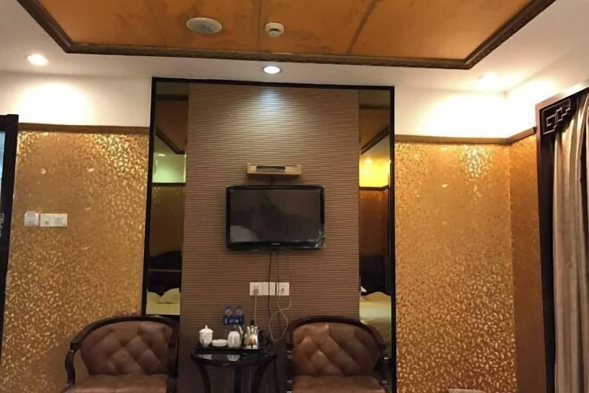 A hotel room with a wooden ceiling, a flat-screen TV mounted on the wall, two leather armchairs, and a small table with a tray of items.