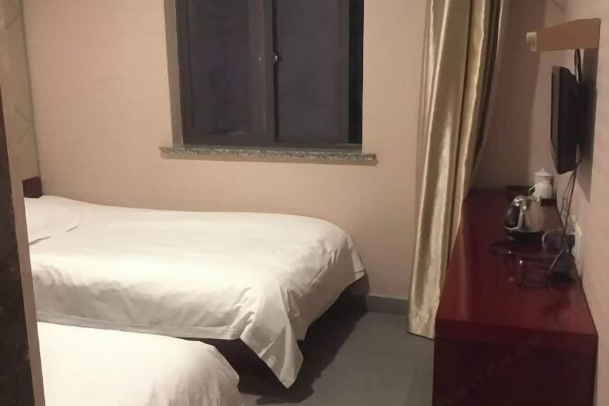 A bedroom with two beds, a window, a TV, and a small table with a kettle.