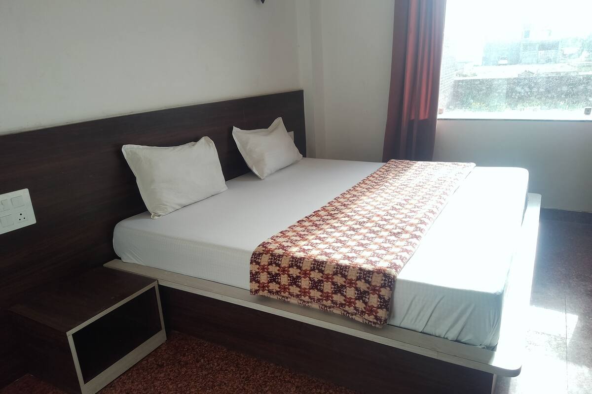 Een netjes opgemaakt bed met een bedsprei met patroon, een houten hoofdbord en een klein nachtkastje.