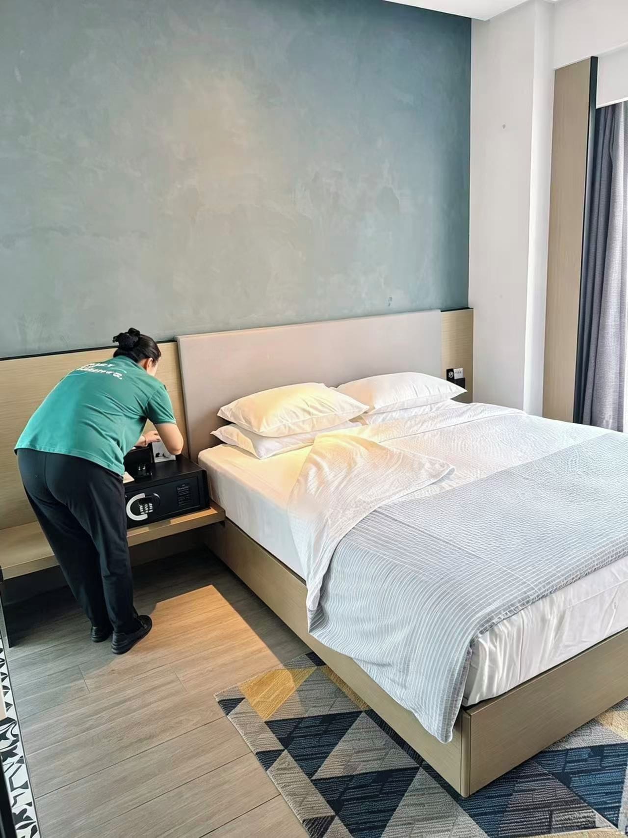 Habitació d'hotel amb un llit, una taula de nit i una persona que arregla el llit.
