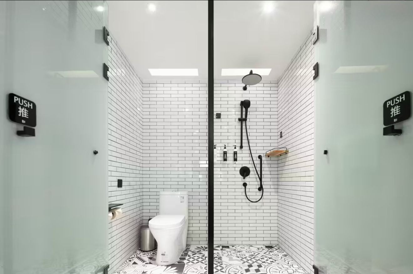 A modern bathroom with white subway tiles, a black shower enclosure, and a toilet.