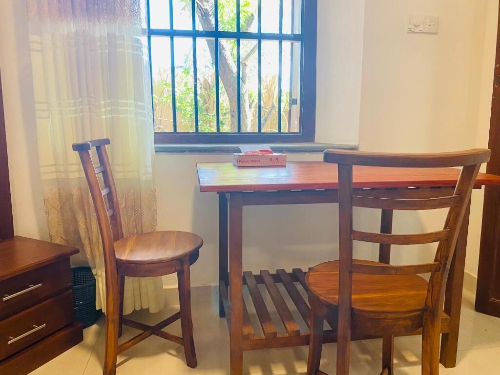 A room with two wooden chairs and a small table, a window with bars, and a curtain.