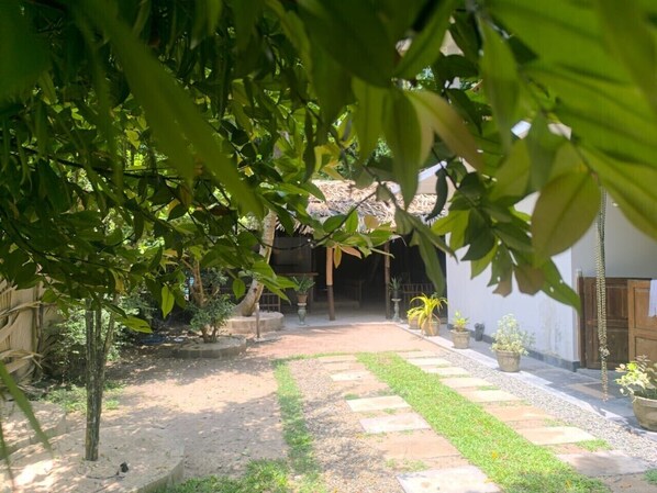 A courtyard with a pathway leading to a building, surrounded by potted plants and trees. - The Horizon Breeze (Ahangama)