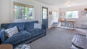 Ein Wohnzimmer mit einem blauen Sofa, einem Esstisch mit Stühlen und einer Tür mit Glasfenster.