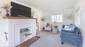 Ein Wohnzimmer mit Kamin aus weißem Mauerwerk, einem Flachbildfernseher, einem blauen Sofa und einem kleinen Beistelltisch.