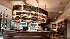 Un bar moderno con una barra curva, varias pantallas y una zona de estar con mesas y sillas.