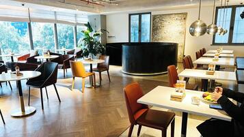 A modern dining area with multiple tables and chairs, large windows with a view of trees, and a central black circular structure.