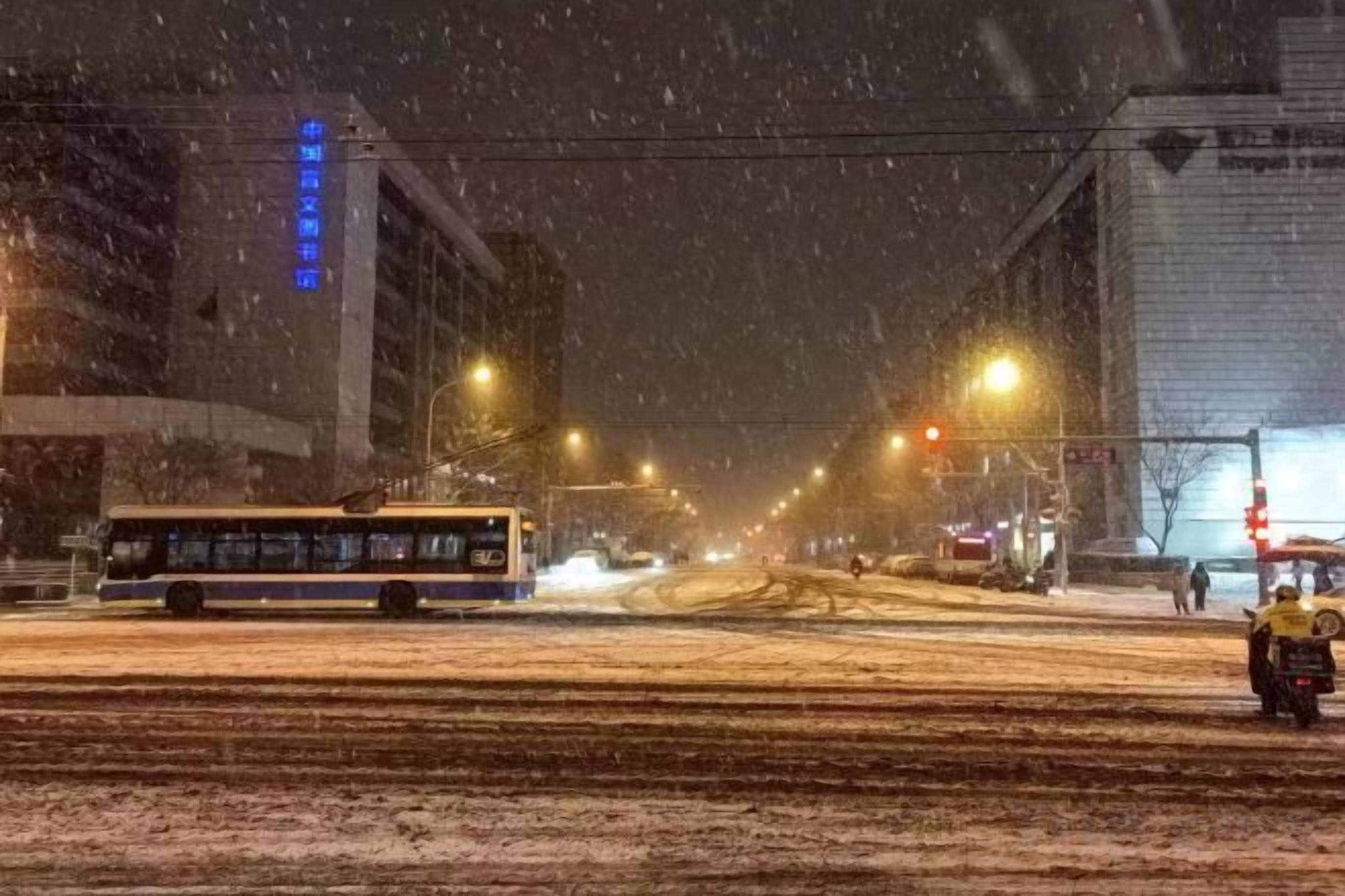 Une scène urbaine enneigée avec un bus, un taxi, des immeubles et des lampadaires.