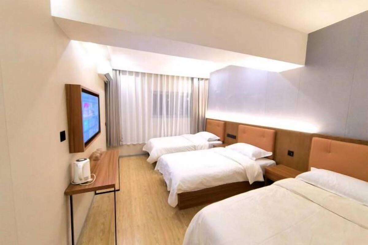 A hotel room with two beds, a small table with a remote control, and a TV mounted on the wall.