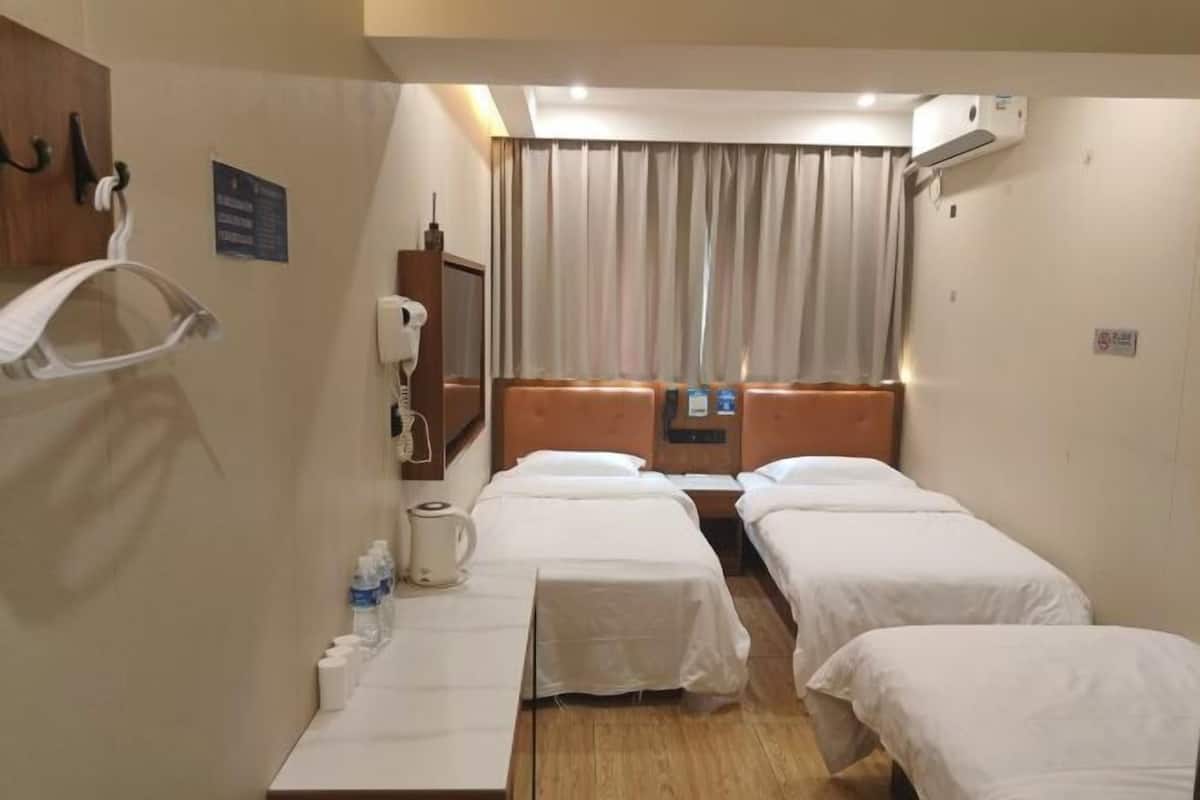 A hotel room with two single beds, a wooden headboard, a small table with a kettle and water bottles, a mirror, and a window with curtains.