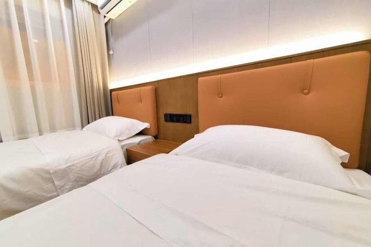 A hotel room with two beds, a wooden headboard, a nightstand, and a wall-mounted control panel.