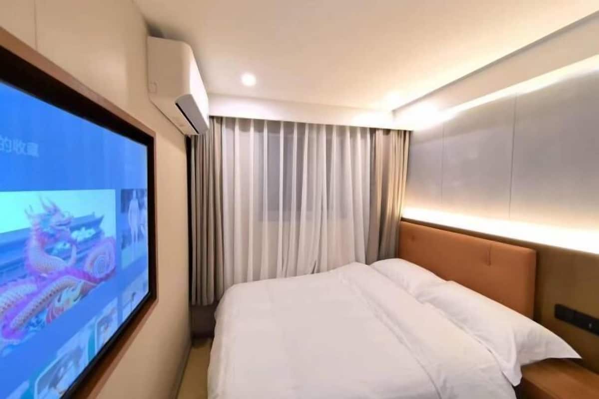 A hotel room with a bed, curtains, a television, and an air conditioning unit.