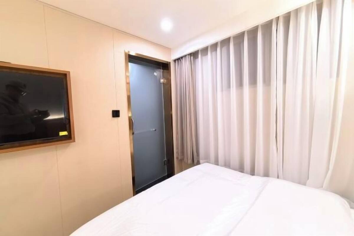 A hotel room with a bed, a door, a mirror, and curtains.