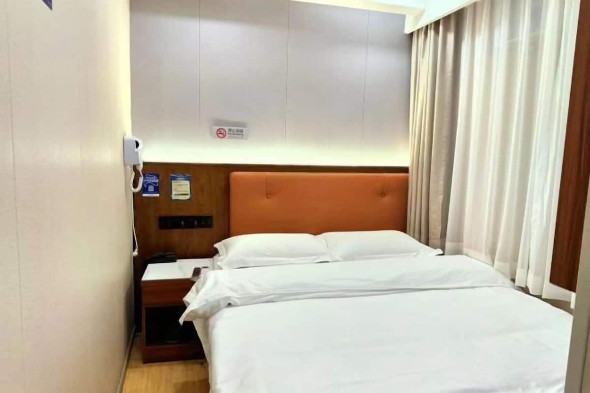 A hotel room with a bed, a nightstand, a wall-mounted phone, and a sign indicating no smoking.