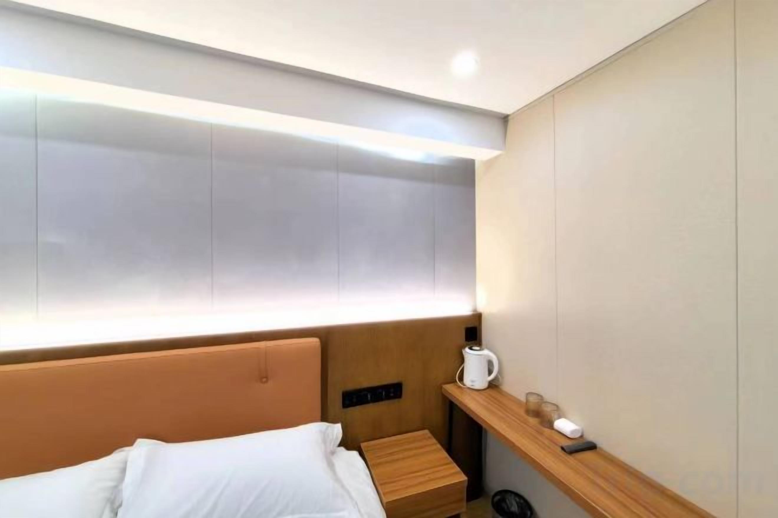 A hotel room with a bed, bedside table, and a nightstand with a lamp.
