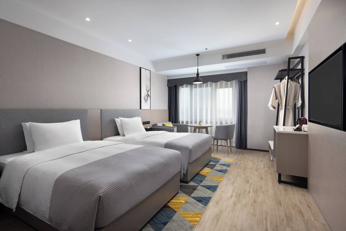 Een hotelkamer met twee bedden, een bureau, een stoel, een televisie en een raam met gordijnen.