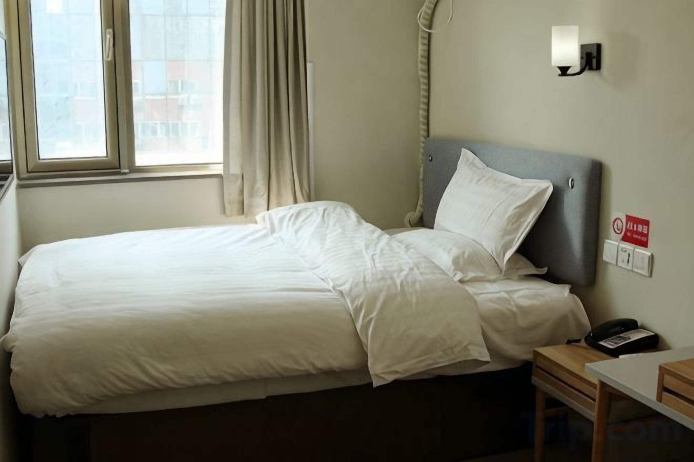 Habitación de hotel con una cama, una mesita de noche, un teléfono y una ventana con cortinas.