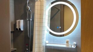 Een moderne badkamer met een douche, een ronde spiegel met verlichting en een handdoekrek.