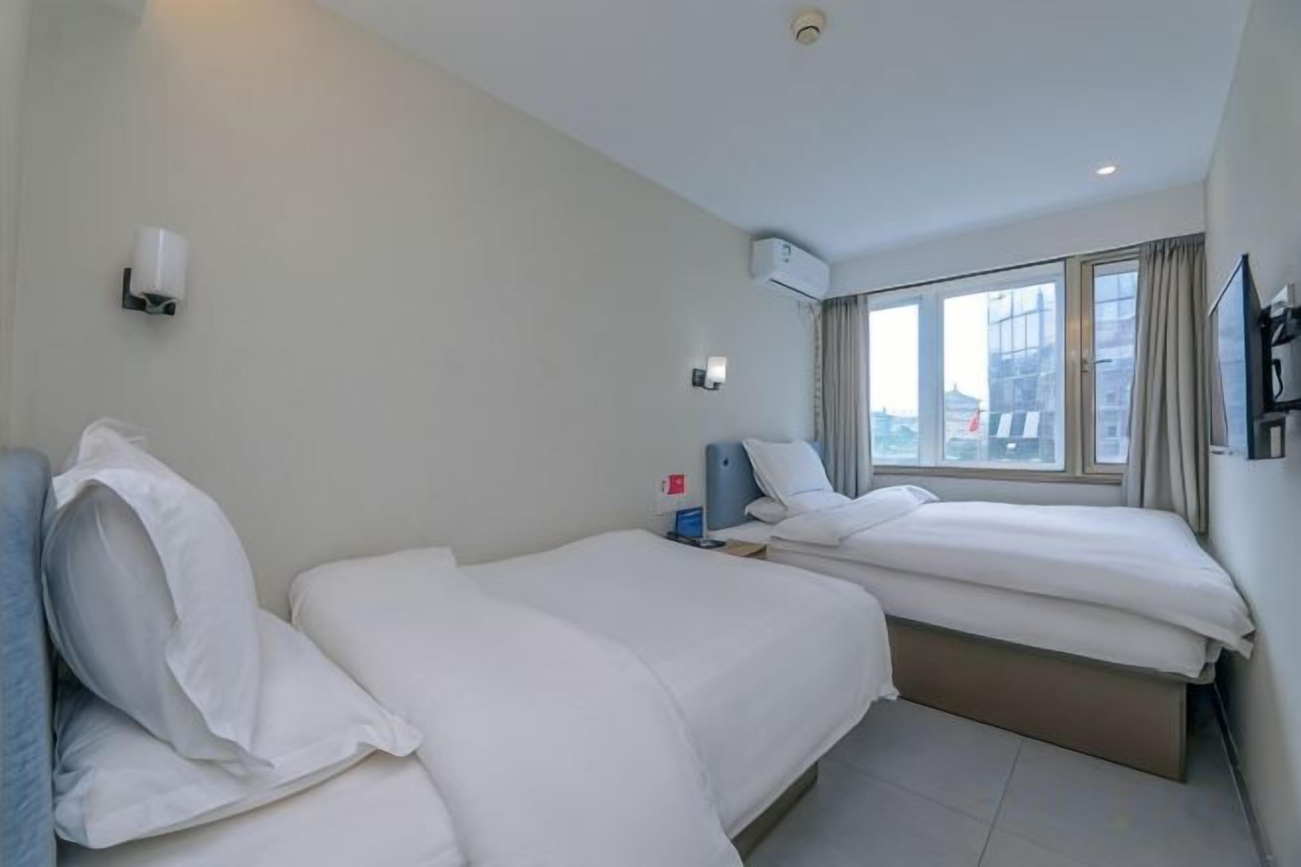 Une chambre d’hôtel avec deux lits, une table de chevet, un climatiseur fixé au mur et une fenêtre avec des rideaux.