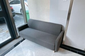 A grey sofa in a room with a tiled floor and a glass door leading outside. - Beijing Bo'an Chain Hotel (Sanlihe Children's Hospital) (Beijing)