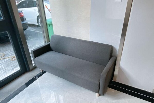 A grey sofa in a room with a tiled floor and a glass door leading outside. - Beijing Bo'an Chain Hotel (Sanlihe Children's Hospital) (Beijing)