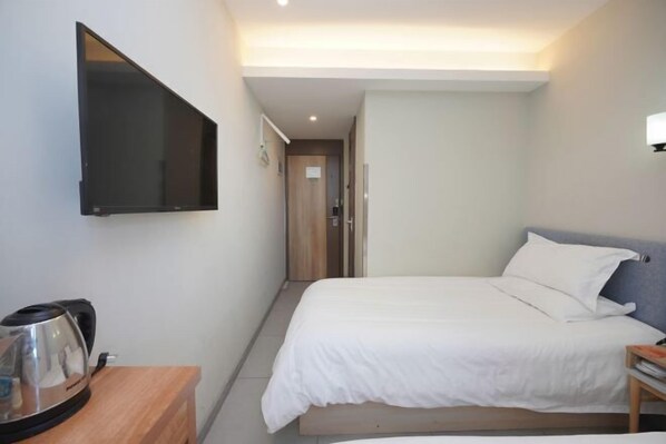 A hotel room with a bed, a TV mounted on the wall, a bedside table with a kettle, and a door leading to another room. - Beijing Bo'an Chain Hotel (Sanlihe Children's Hospital) (Beijing)