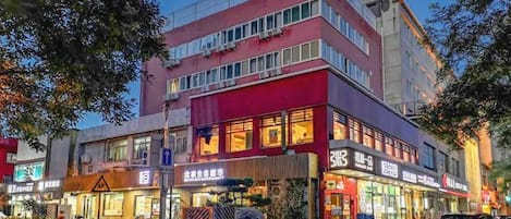 Um edifício com vários andares, com estabelecimentos comerciais no térreo, incluindo um restaurante e uma loja com letreiros em língua estrangeira.