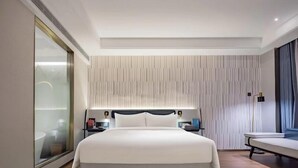Une chambre d’hôtel moderne avec un grand lit, une table de chevet, une commode et une grande fenêtre avec des rideaux.