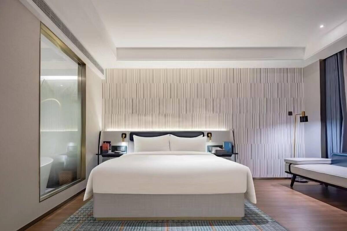 Een moderne hotelkamer met een groot bed, een nachtkastje en een groot raam met gordijnen.