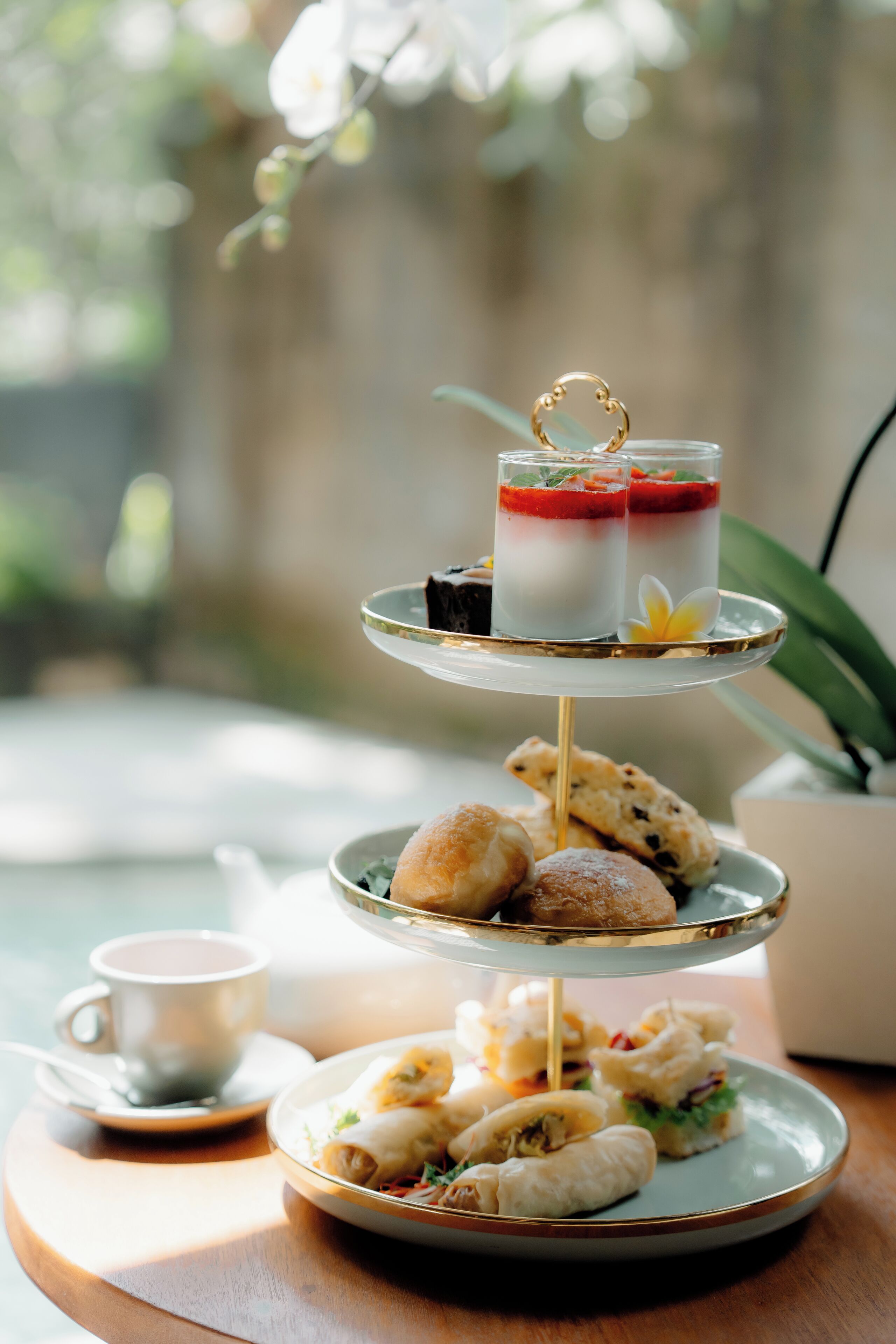 A three-tiered dessert stand with pastries and a cup of tea on a wooden table.