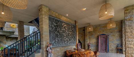 A lobby with a stone wall, a staircase, a wooden table, and hanging lights.
