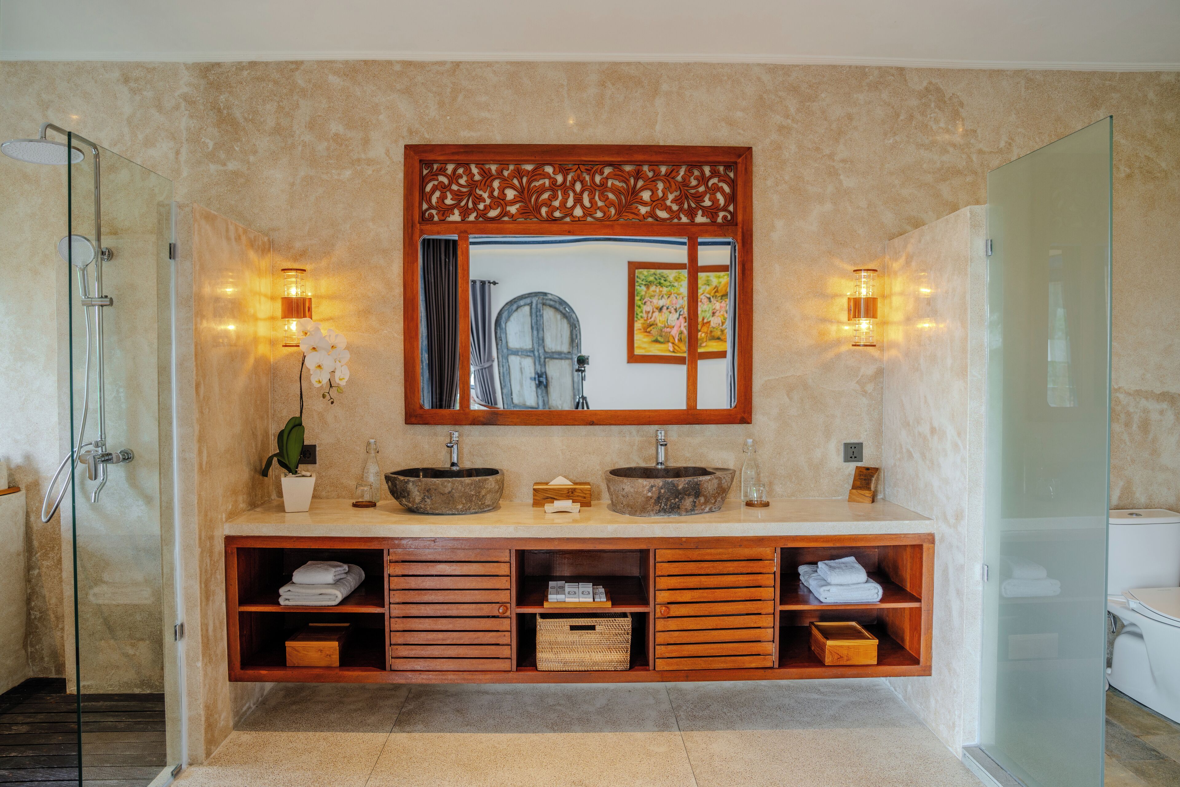 A modern bathroom with a glass-enclosed shower, a wooden vanity with two sinks, and built-in shelves.