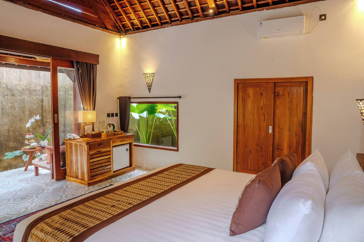 A bedroom with a bed, wooden wardrobe, bedside table, and a view of a garden through a sliding door.