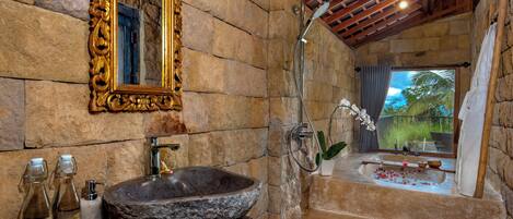 A bathroom with a stone sink, a large mirror, and a shower.
