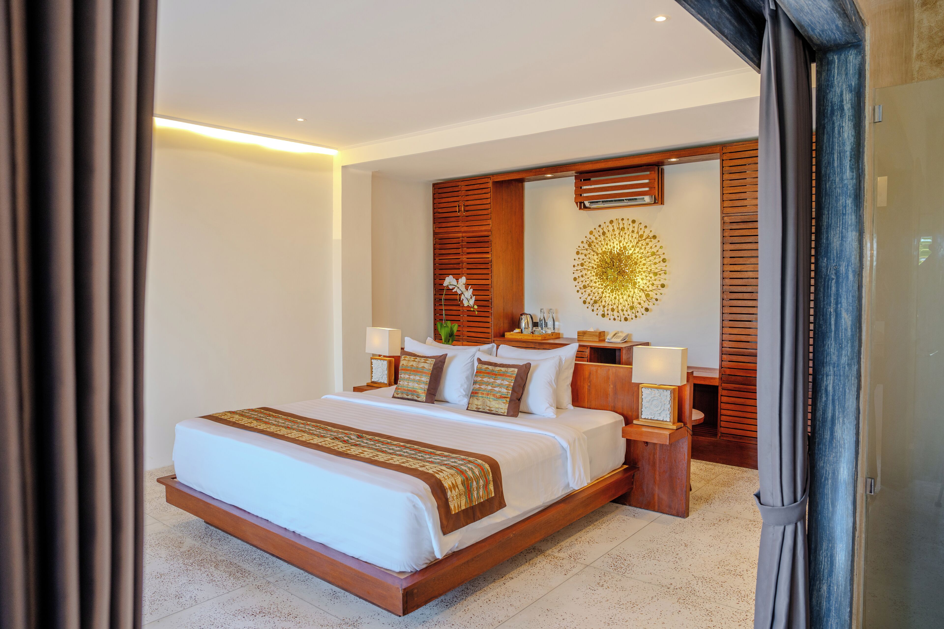 A spacious bedroom with a large bed, wooden headboard, bedside tables with lamps, and a decorative wall piece.