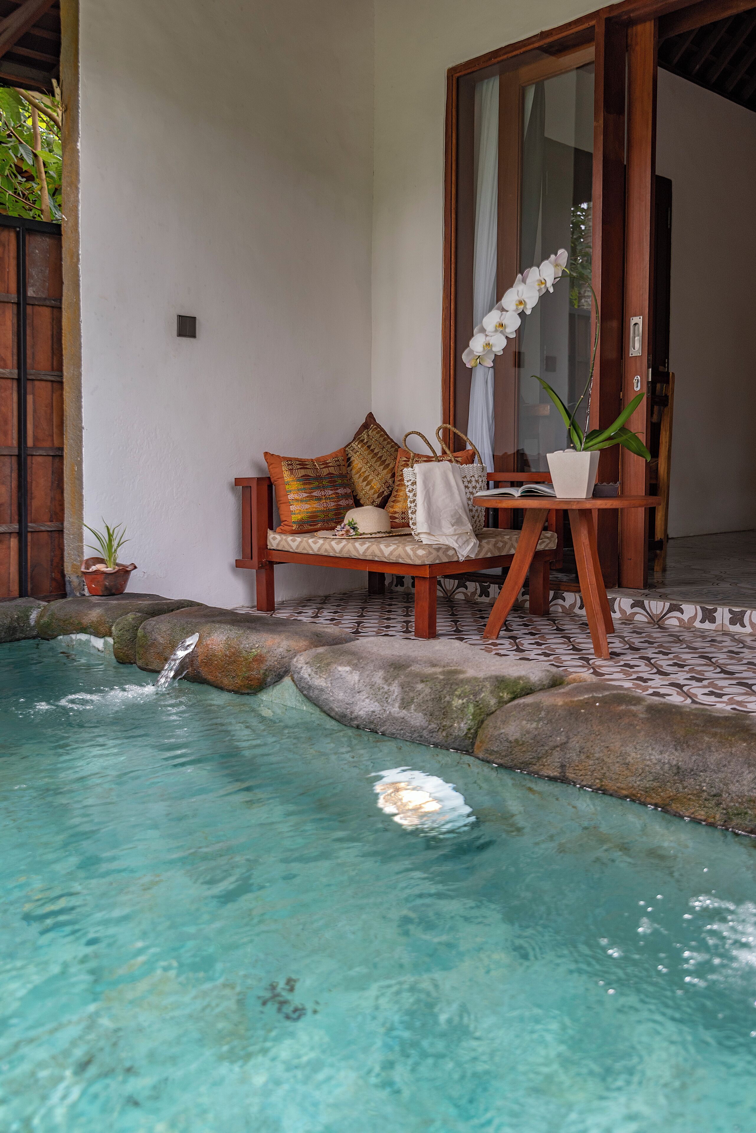 A pool area with a wooden bench, a potted plant, and a small waterfall.