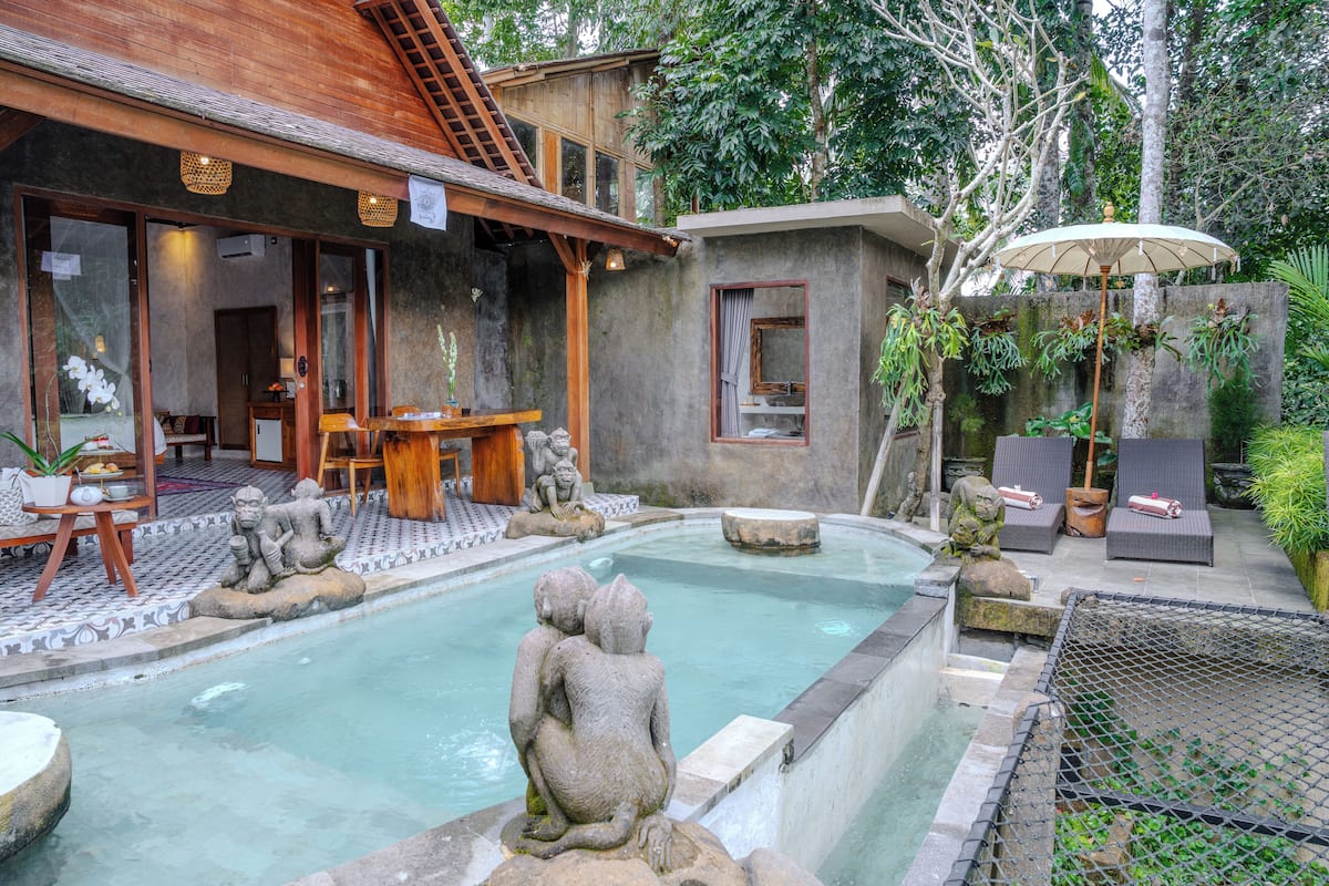 A pool area with stone sculptures, a wooden deck, and a covered seating area with umbrellas.