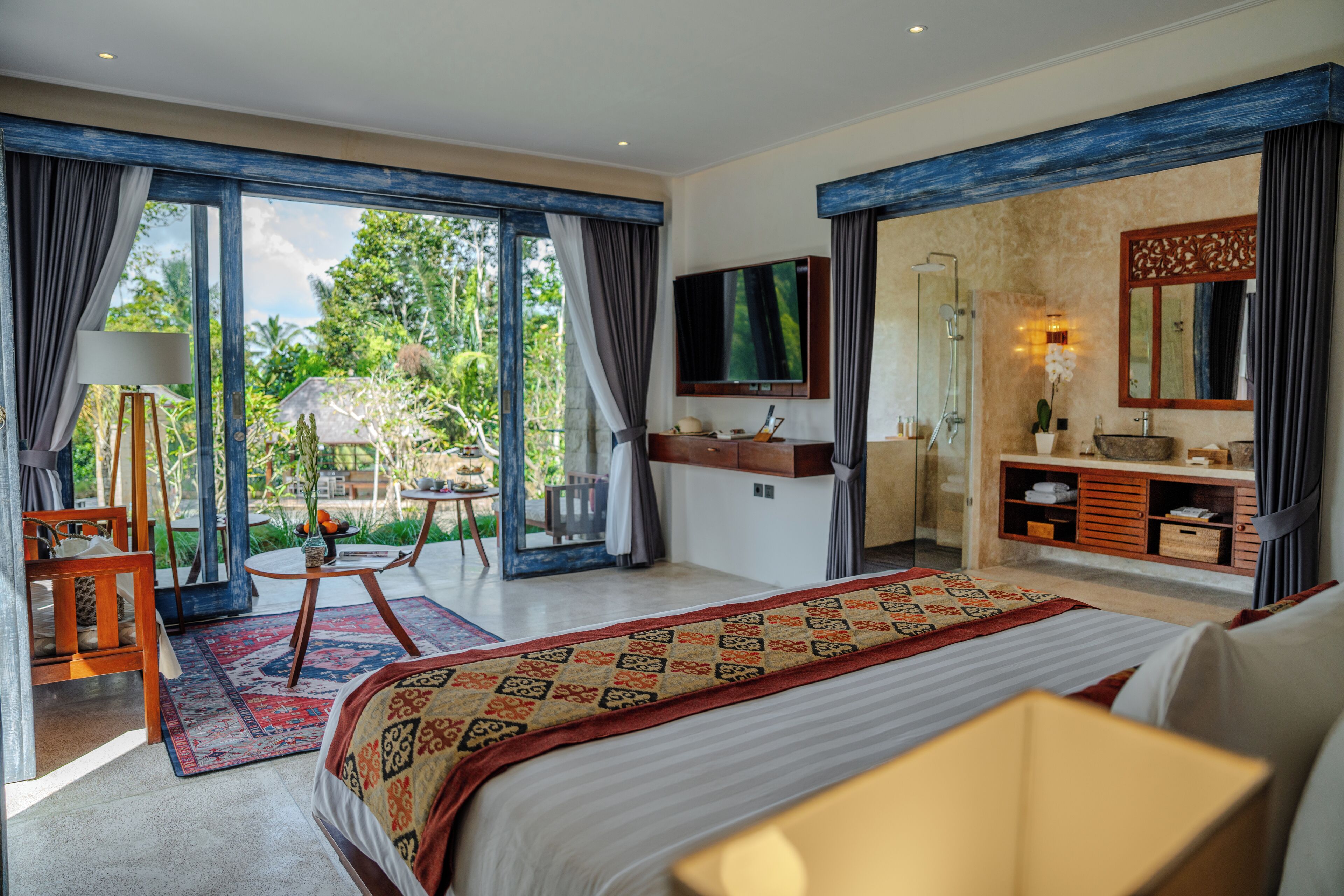Um quarto espaçoso com uma cama grande, televisão, banheiro com chuveiro e varanda com vista para o exterior.